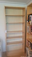 Full front view of the light wood Ikea Billy bookcase with six shelves, empty and against a wall beside another bookshelf.