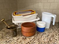 Lot contents on granite counter including brass mortar and pestle, wooden bowls, thermos, milk bag holder, and plastic storage bins.