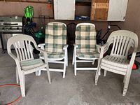 Wide view of six plastic chairs in garage area, including two white reclinable chairs with checkered cushions and four beige stackable chairs with striped cushions.