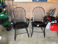 Front view of two black wooden Windsor style armchairs with spindle backs and curved armrests.