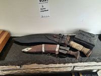 Photo showing two collectible cutting knives lying on a dark stone surface alongside the metal box and a wooden item partially visible.