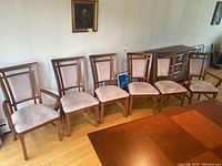 Six chairs arranged in a row with table in foreground, showing wood frames and beige upholstered seats and backs.