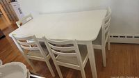 Full view of the white painted rectangular wooden dining table with four matching chairs around it on a hardwood floor.