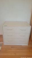 Front view of the white three drawer dresser showing all drawers and handles.