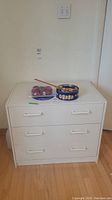 Front view showing the dresser with three drawers and white handles, a tin and a small item placed on top.