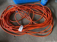 Coiled heavy-duty orange extension cord lying on a concrete floor.