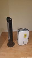 Both the AeonAir white dehumidifier and Seville Classic tower fan shown side by side on a wooden floor against wall