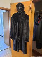 Photo of the full mink coat and matching hat hanging on a wooden door, showing the coat's length and fur texture.