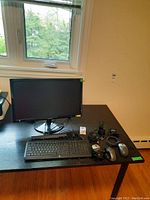 Samsung 24" monitor, HP keyboard, Dell and Logitech mice, laptop battery on black table under window light.