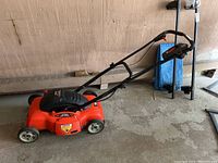 Side view of red electric mower with black handle in garage