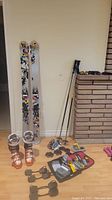 Full lot on laminate floor against white wall showing boots, skis, poles, goggles, glasses, and waxing kit