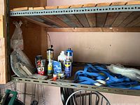 Shelf with car chemicals including WD-40 and other spray cans, small packed hardware items, and blue tow straps.