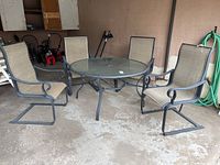 View of the full patio set showing the round table with glass top and four matching chairs around it.