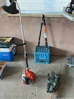 Full view of Echo GT225 string trimmer, Fiskars loppers on milk crate, green pruning shears on floor, Black and Decker TR165 hedge trimmer leaning on window sill in garage