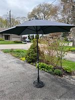 Umbrella fully unfurled outdoors on driveway with plants and house in background