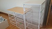 Wide angle photo showing three white metal wire shelving units with wooden tops, displaying their structure and condition.