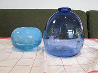 Two blue glass vases side by side on a white and red checked cloth, showing size and form differences