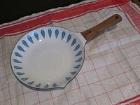 Top side of skillet showing white enamel surface with blue lotus pattern around edge and wooden handle.