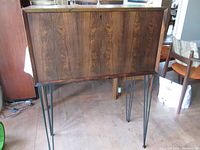 Front view of closed rosewood bar unit with metal hairpin legs on a wood floor