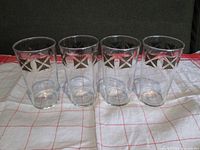 Set of four clear cylindrical bar glasses featuring a repeated black and gold pirate flag design near the rim, arranged in a row.
