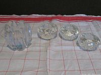 Four clear glass mid century modern candle holders on a white and red checkered cloth: three mushroom-shaped taper holders with textured bottoms and one artichoke-shaped tealight/votive holder.