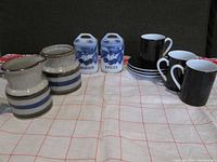 Overall view of 10 ceramic pieces including 2 striped pottery pieces, 2 blue and white spice jars, and 3 black cups with 3 saucers.