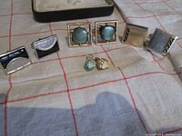 Photo showing three pairs of cufflinks and two small Faberge egg pendant drops arranged on a cloth.