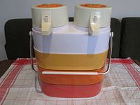 Front view of the beverage server showing two white pump dispensers and the colorful metal body with horizontal stripes in white, yellow, and orange/red.