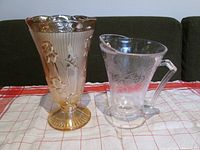 Pressed glass vase and clear glass pitcher on a cloth with a couch in background