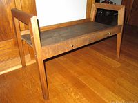 Side angled view of the wooden stand showing the wood grain, legs and handle extensions on each end.