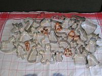 Photo showing the full lot of over 30 metal cookie cutters laid out on a checked cloth, featuring Christmas and Easter shapes like stars, candy canes, bunnies, and gingerbread men.