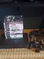 Photo of the PlayStation 2 console with the stack of 14 PlayStation 2 game cases on top, also showing part of the controllers to the right.