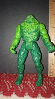 Front view of Swamp Thing 1990 Kenner Toys action figure with a ruler showing 5.5 inches tall. Figure is green with detailed textured body.
