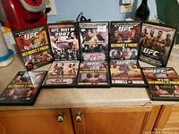 Photo of 10 UFC DVD cases displayed on a counter, showing various Ultimate 2 Pack editions and individual UFC event DVDs.