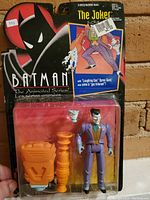 Photo of the Batman: The Animated Series Joker action figure in original packaging, showing figure and accessories in blister pack against branded card with logo and artwork.