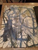Photo of abstract painting side with blue, gray, and olive green acrylic paint drips and splatters on white art paper.