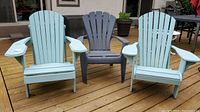 Three Adirondack-style chairs on wooden deck: two painted light blue wooden chairs showing paint peeling and weathering, one gray resin chair.