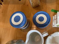 Top view of two blue and white striped ceramic jars with concentric circle patterns on lids and sides, showing their design and scale relative to the surrounding floor and other items.