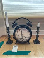 Clock flanked by two metal candleholders each with a candle, showing overall lot contents and condition with tarnish and wax drippings on candles.