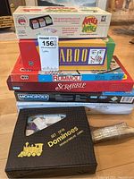 Stack of boxed games including Apples to Apples, Taboo, Rummoli, Scrabble, Monopoly, Harry Potter, and boxed Dominoes set