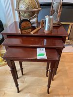 Frontal view of the three size-varied wooden nesting tables stacked together showing dark reddish-brown wood finish and carved tapered legs.