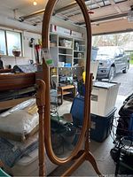 Full view of the oval wooden framed standing mirror showing the mirror adjustable tilt and overall structure.