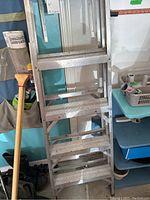 Full view of the Featherlite aluminum step ladder showing the steps and surrounding environment with adjacent broom and household items.