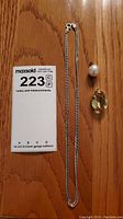 Photo of necklace chain alongside two pendants on a wood surface with auction lot number card