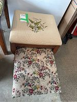 Side view of beige fabric cushioned stool with needlepoint floral design on top and wooden legs, showing floral embroidery on top.