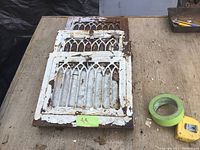 Three vintage cast iron air registers stacked on a wooden surface showing wear and paint chipping