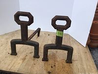 Front and side view of both cast iron andirons with a hexagonal handle top and sturdy base.