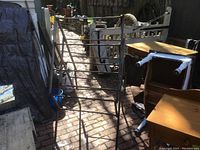 Antique wooden quilt rack positioned outside on brick ground near various furniture pieces.
