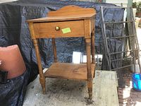 Front view of antique wash stand showing drawer and shelf, wooden frame with turned legs and brass knob.
