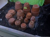 Multiple terracotta clay pots arranged on a surface. Varied sizes and stacked groupings visible with drainage holes visible on top of some pots.
